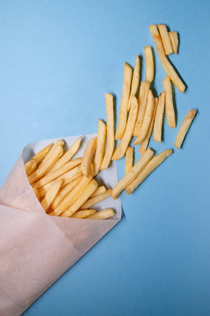 Crispy French fries spilling from paper on a bright blue background.