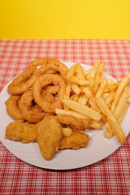High angle of fried potato with onion rings and nuggets on plate on table near yellow wall
