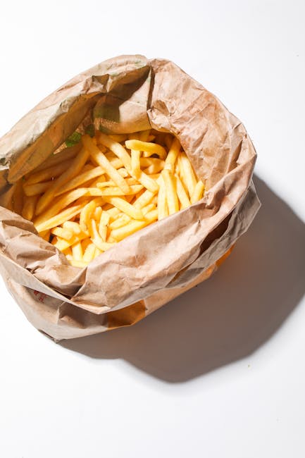 A delicious serving of golden crispy french fries in a rustic brown paper bag on white background.