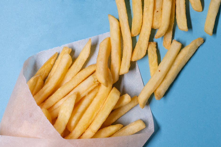 Top view of tasty french fries in paper placed on blue table in light studio