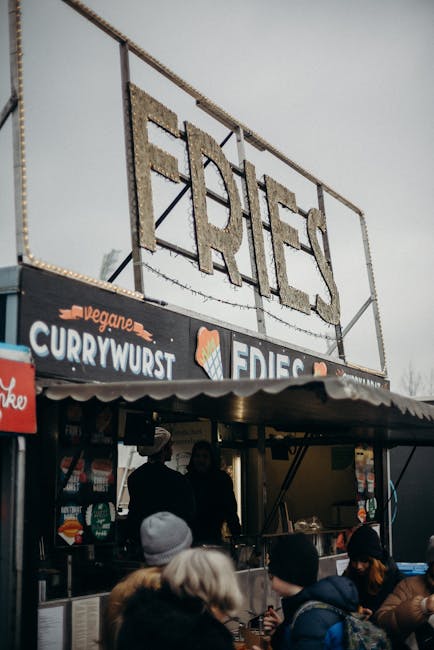 Outdoor street food stall offering fries and vegan currywurst at a market.