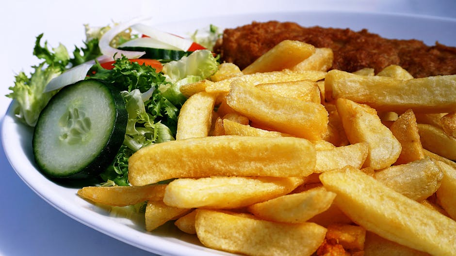 Golden fish and chips served with a fresh cucumber and lettuce salad on a plate.