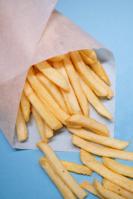 Freshly fried French fries spilling from paper on a vibrant blue background.
