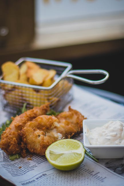 Close-up of crispy fish and chips with tartar sauce and lime on newspaper.
