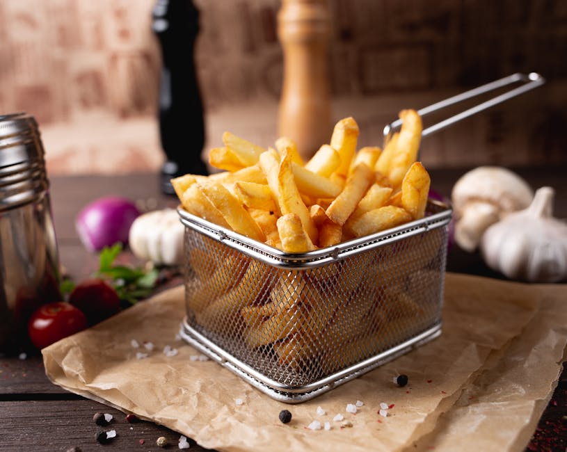 Composition of appetizing fresh french fries in steel basket placed on table amidst garlic and mushrooms