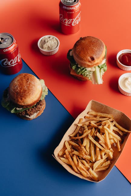 Appetizing fast food flat lay with burgers, fries, and sodas on a vibrant background.