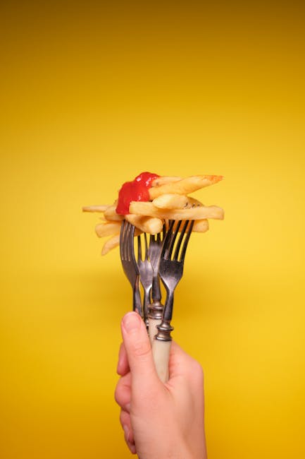 Crop anonymous person hand with forks with fried potatoes and ketchup on yellow background in bright studio