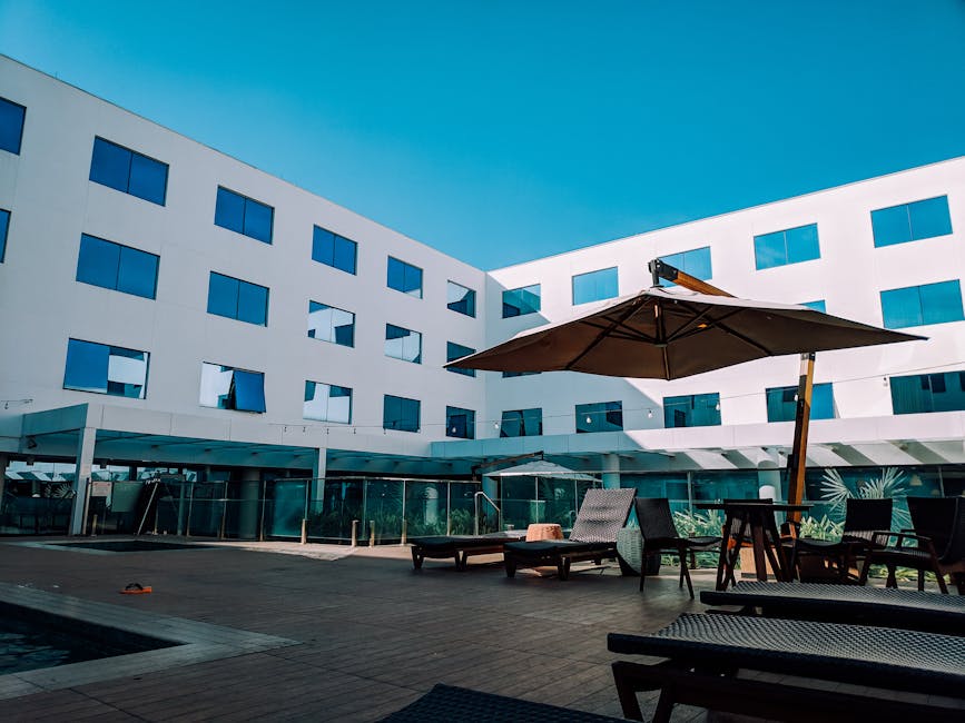 Spacious hotel courtyard featuring modern architecture, lounge chairs, and an umbrella under a clear blue sky.