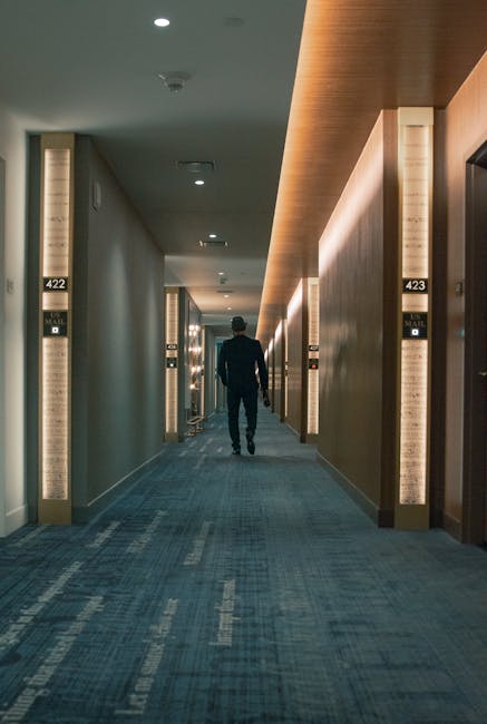 A person walking down a well-lit hotel corridor with room numbers and modern design.