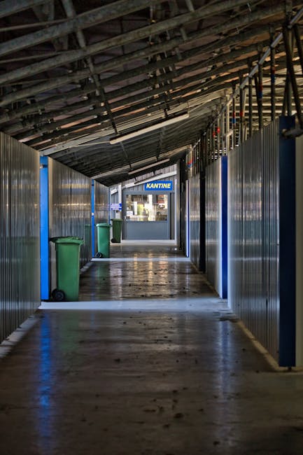 Deserted industrial corridor with trash bins leading to a canteen at the end.