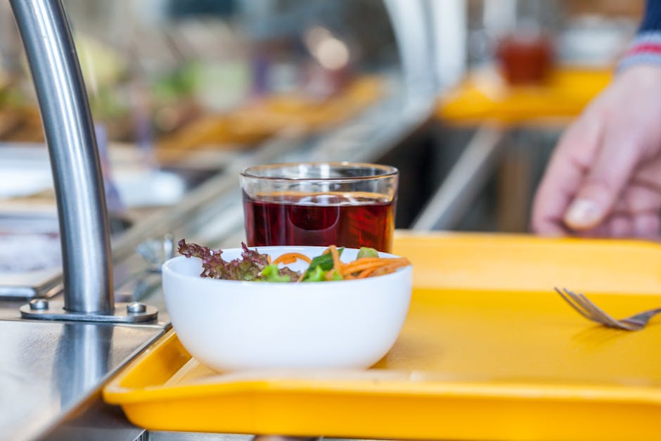 Crop unrecognizable person with bowl of delicious salad and glass of refreshing drink in self service restaurant