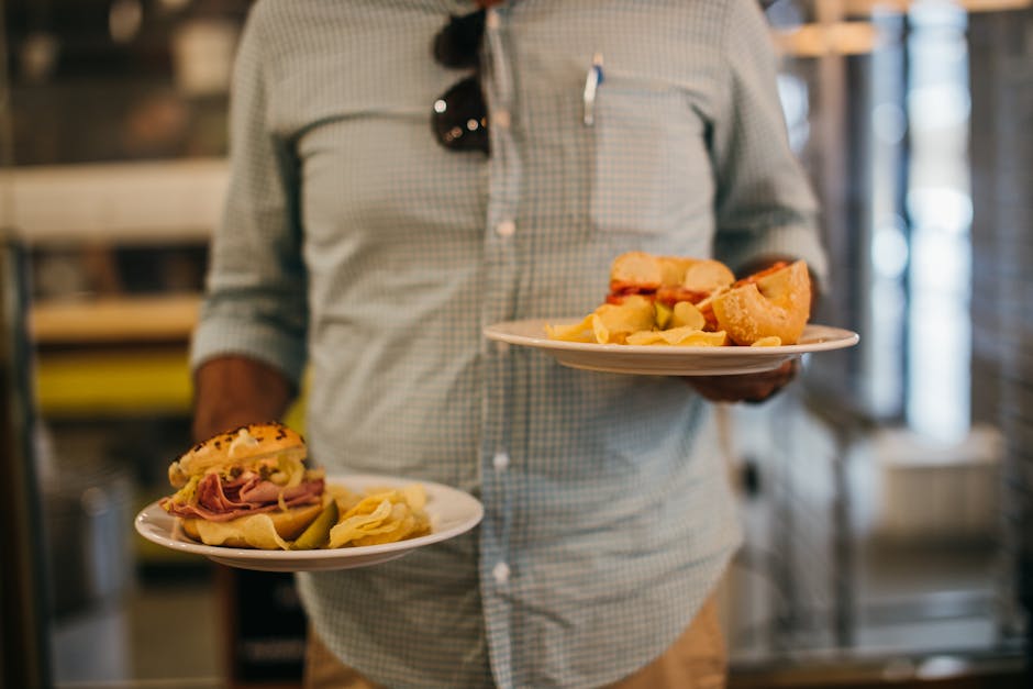 Casual dining scene with sandwiches and chips held by man in plaid shirt.