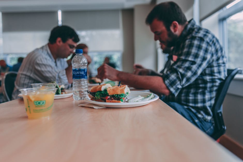 Two men enjoying a casual lunchtime in the office with sandwiches and orange juice.