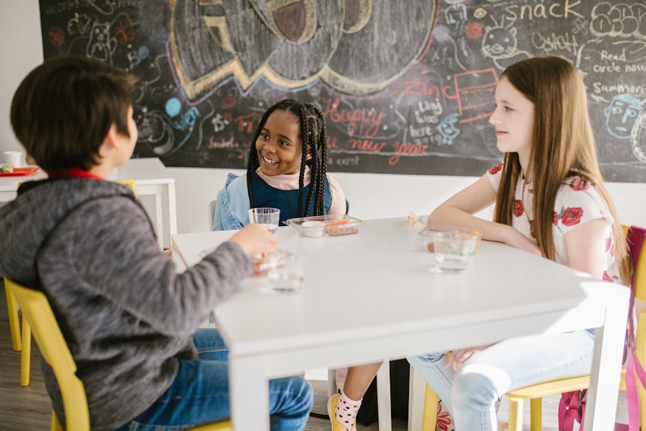 Three children engage in lively conversation during snack time at school.