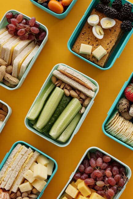 An assortment of colorful lunch boxes with fruits, vegetables, and snacks on a vibrant yellow background.