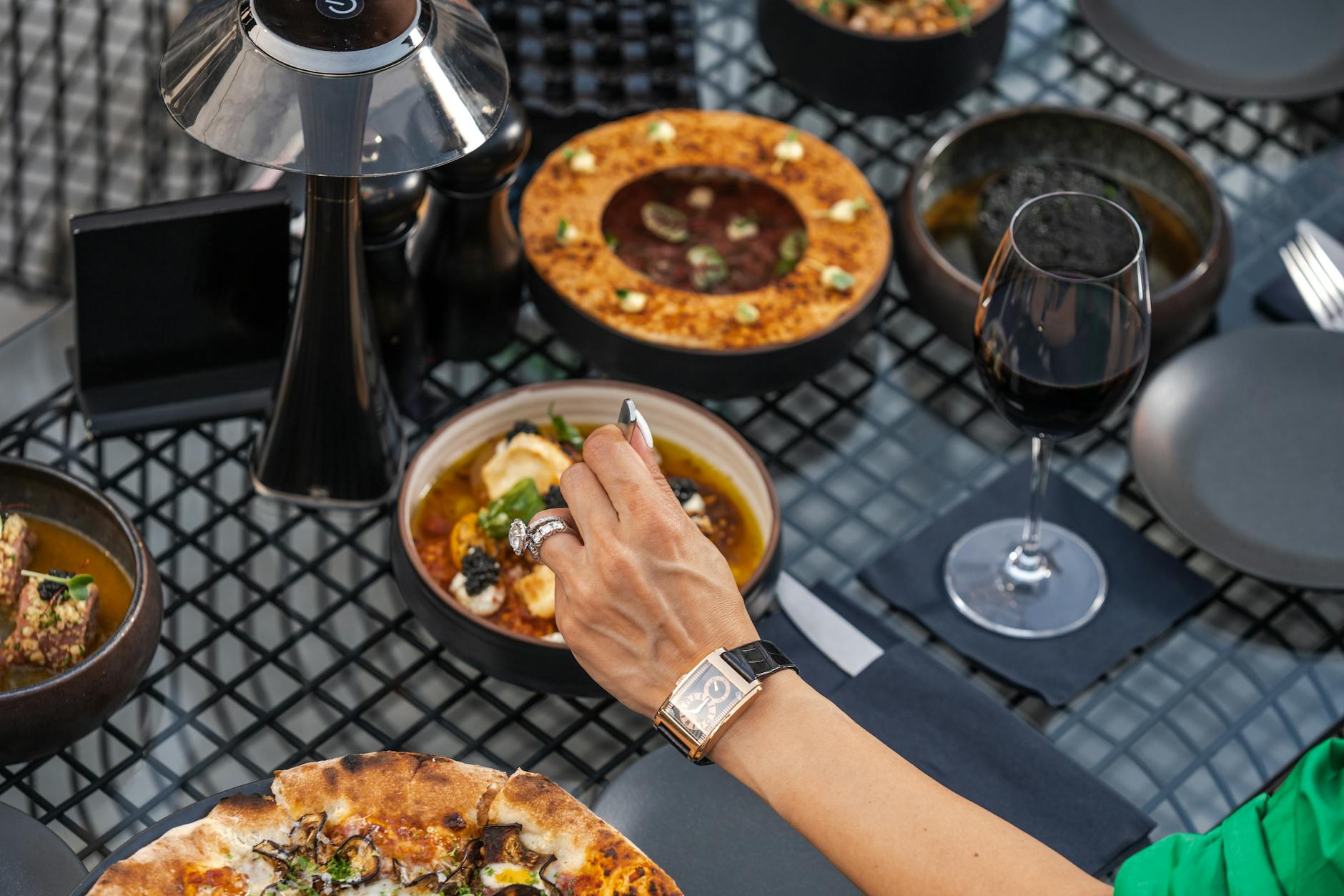 Een luxe diner setting met diverse gerechten, wijn en een elegante damesarm met horloge en ring.