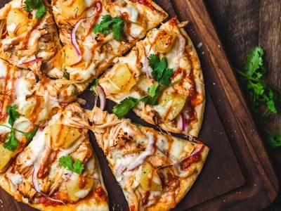 Een heerlijke pizza met ananas, kip en koriander op een houten plank, perfect voor een zakelijke lunch.