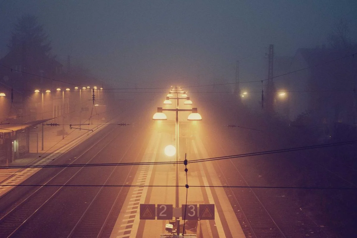 Sfeervolle foto van een mistig treinstation in de avond met warme verlichting.