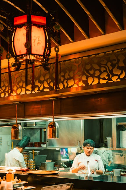 Chefs preparing dishes in a stylish Asian restaurant kitchen with warm lighting.