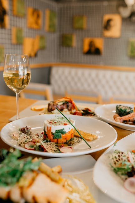 Served table with various delicious dishes and glass of white wine in modern restaurant on blurred background