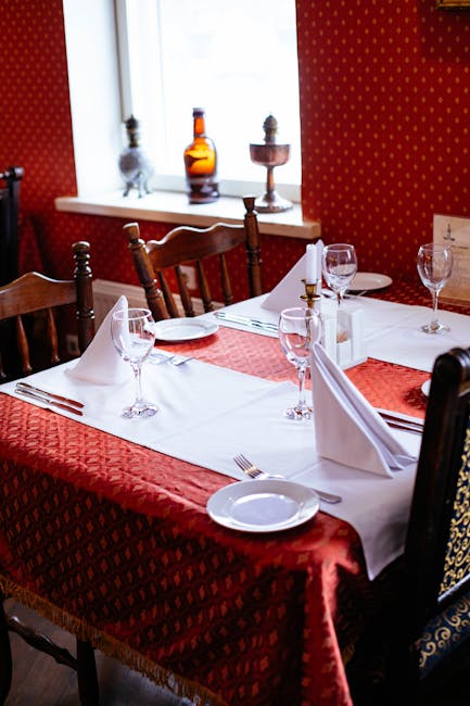 Chic table setup with red tablecloth, glassware, and napkins in a warm-toned restaurant.