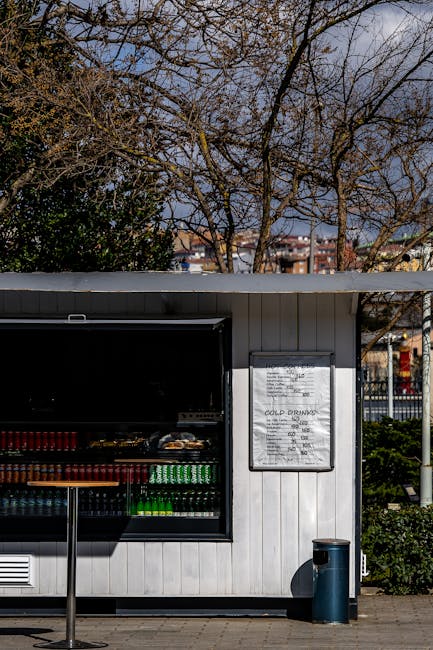 A wooden outdoor beverage stand offering cold drinks amidst a scenic backdrop of leafless trees.