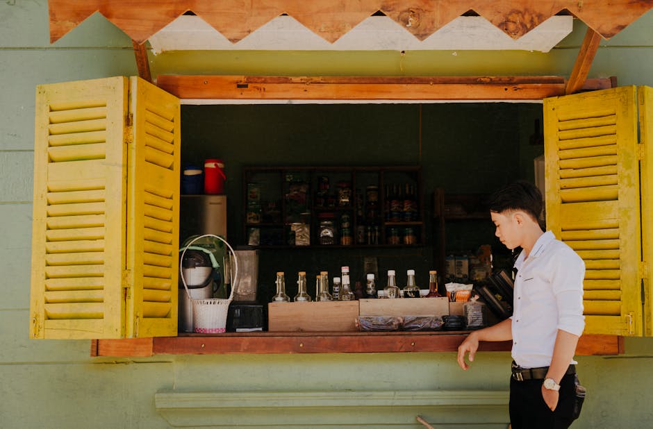 A young man standing beside an open street shop window with beverages displayed inside.