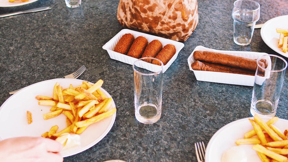 A casual lunch setting featuring french fries, sausages, and croquettes on a table with glasses.