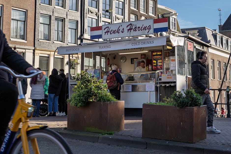 Een foodtruck genaamd Henk's Haring in een levendige Amsterdamse straat met mensen en een fietser.