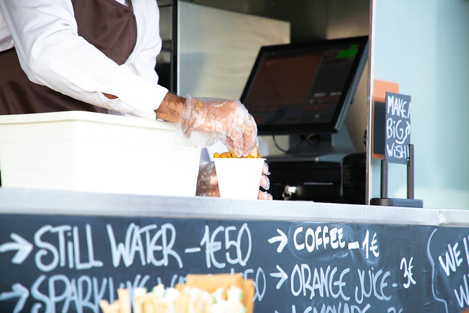Low angle of crop anonymous male seller with cup of fried food at counter with cashier