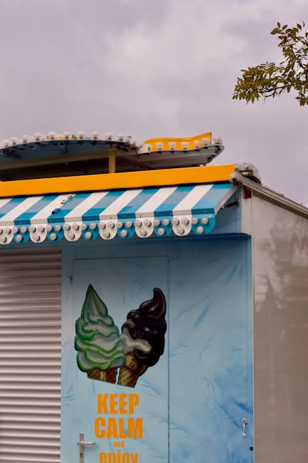 Colorful ice cream kiosk with a striped awning and 'Keep Calm' sign under a cloudy sky.