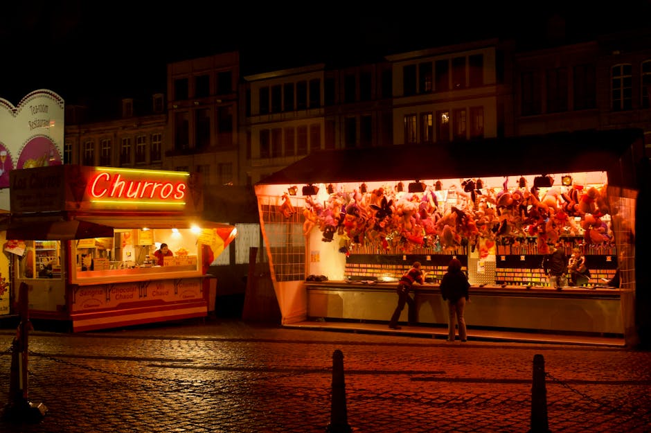 Illuminated churros stand and festival game stall at night in a vibrant street setting.