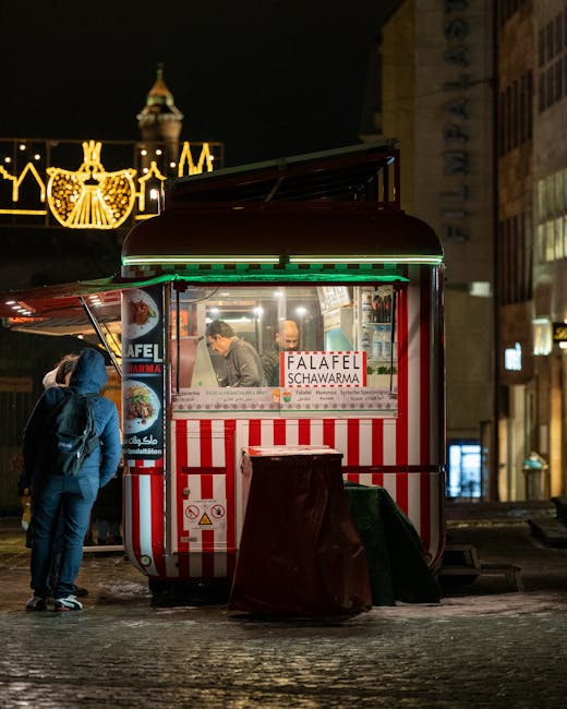 Cozy night scene with people ordering at a falafel and shawarma cart on a bustling city street.