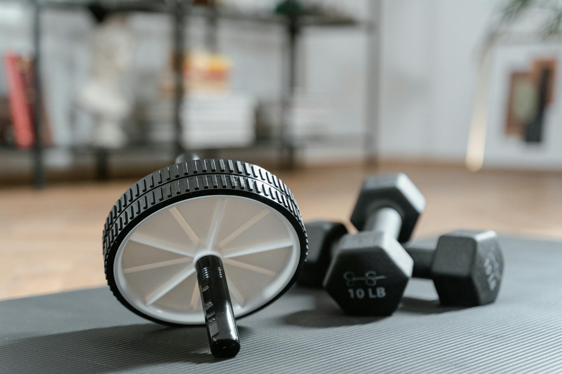 Een ab roller en twee dumbbells van 10 lb liggen op een grijze fitnessmat.