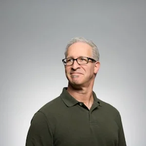 Portret van een man met bril en grijzend haar, gekleed in een groene polo.