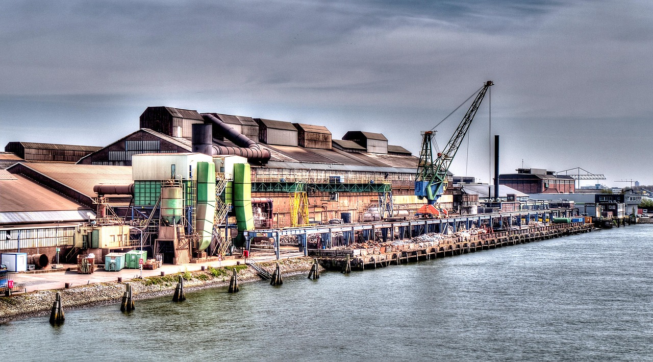 Industrieel havengebied met kranen en gebouwen langs het water onder een bewolkte hemel.