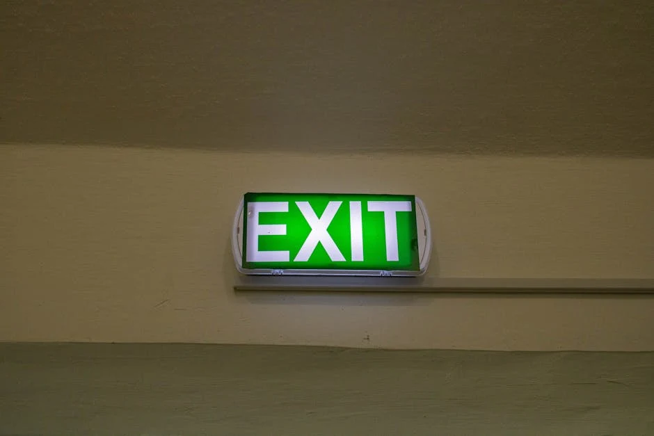 Een groen verlichte exit-bord hangt aan een beige muur in een gebouw.