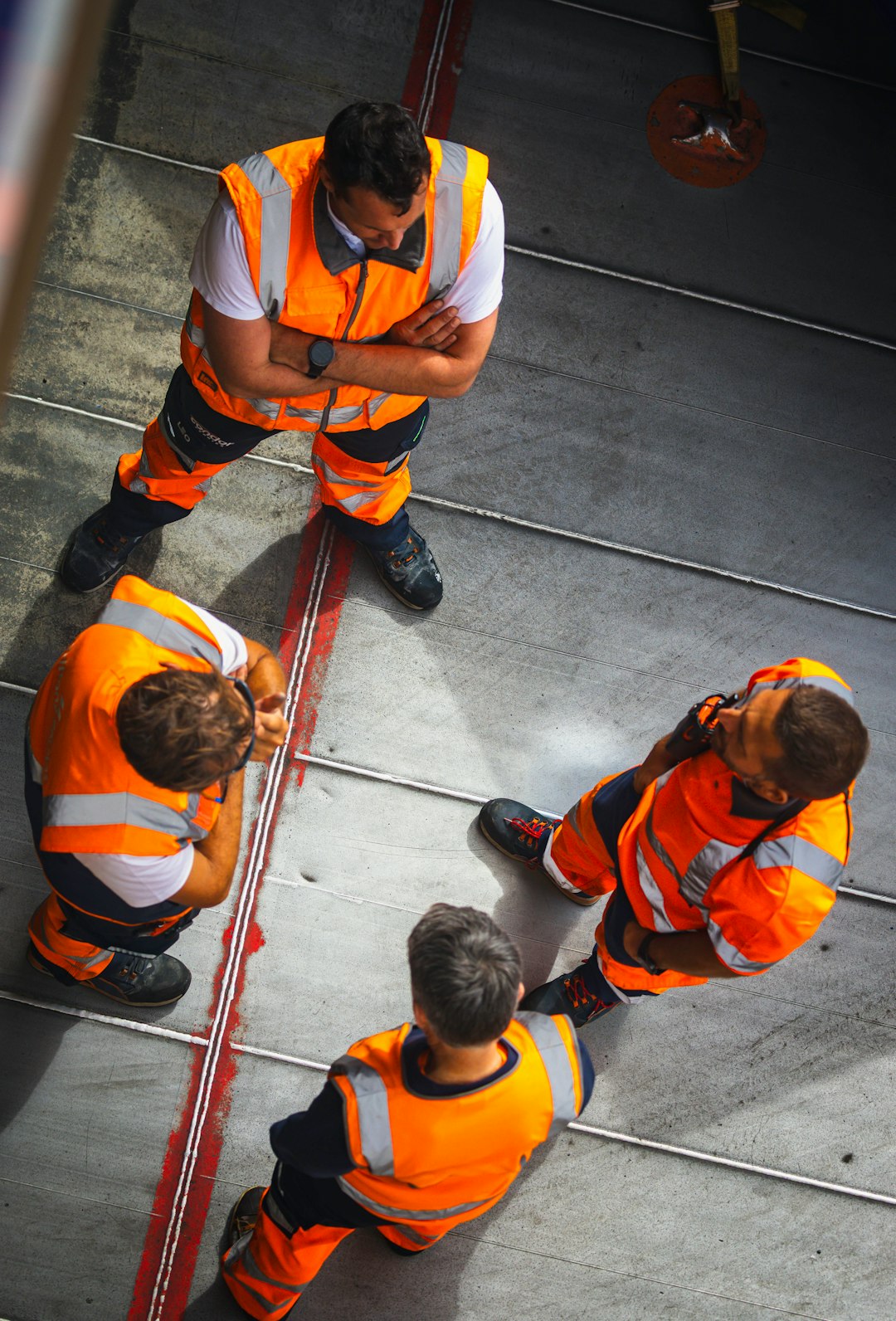 Four workers in orange high-visibility vests standing on a grey industrial floor