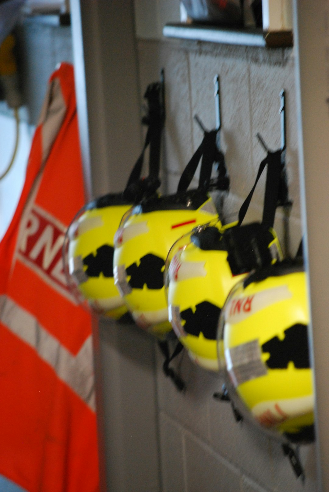 Four yellow safety helmets with clear visors hanging on hooks against a wall